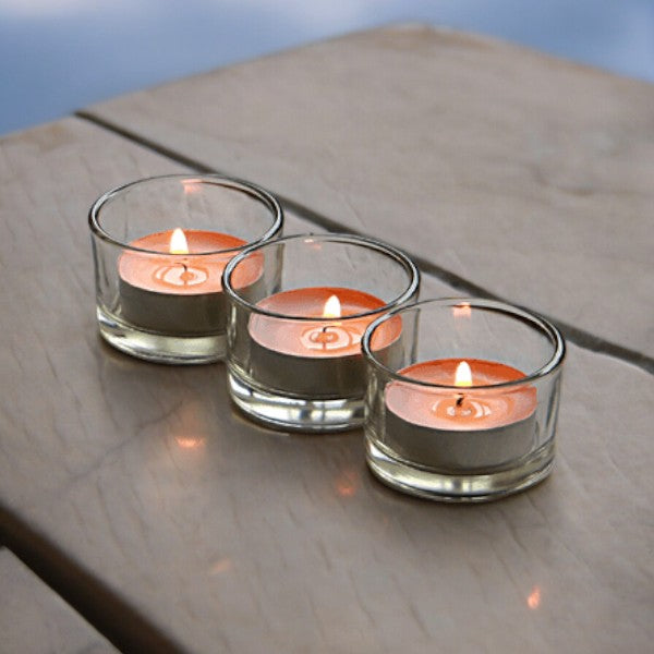 Three clear glass tealight holders with lit candles on a wooden table