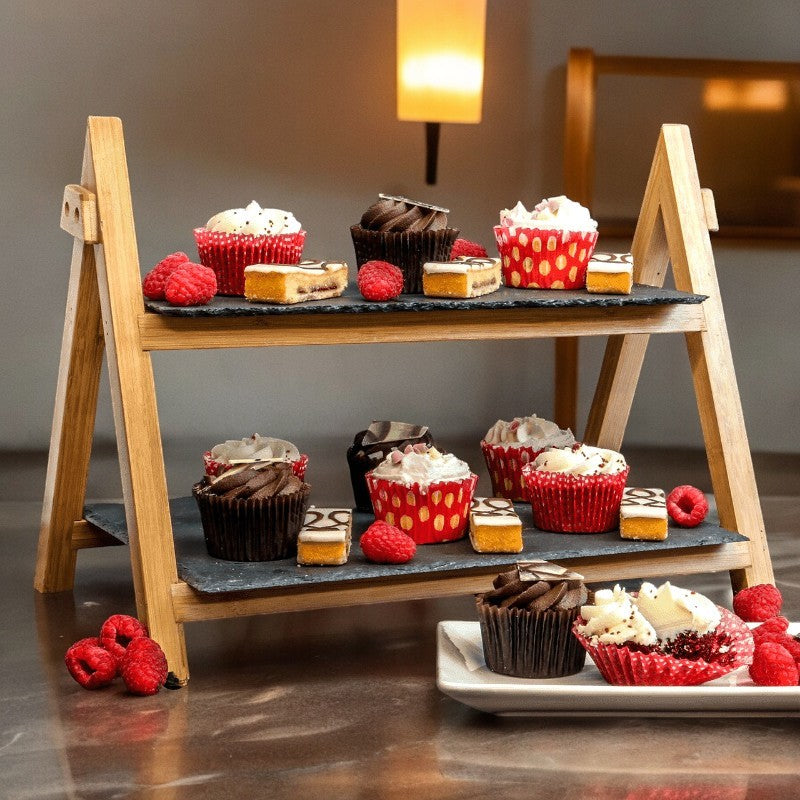 Two-tier bamboo and slate cake stand displaying cupcakes