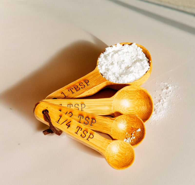 Four bamboo measuring spoons with engraved measures, shown with flour