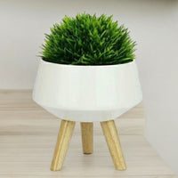 White faceted ceramic plant pot on three wooden legs, styled with a plant not included