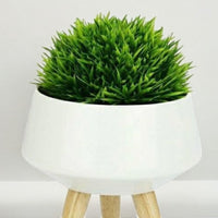 Close-up of the white ceramic planter and wooden legs, with display greenery