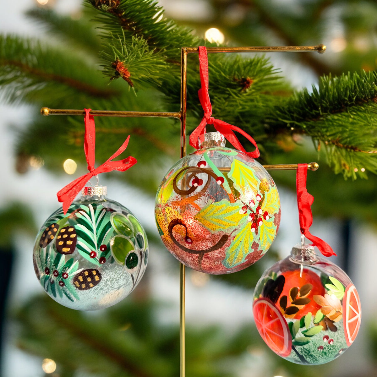 Three hand-painted glass baubles hanging from red ribbons on a Christmas tree