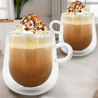 Two double-walled coffee mugs topped with cream and caramel