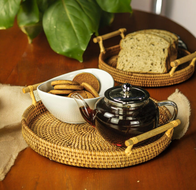 Two round rattan serving trays holding bread, a teapot and a small bowl