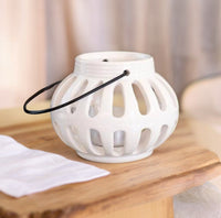 White ceramic tealight lantern with cut-out pattern and dark handle on a wooden surface