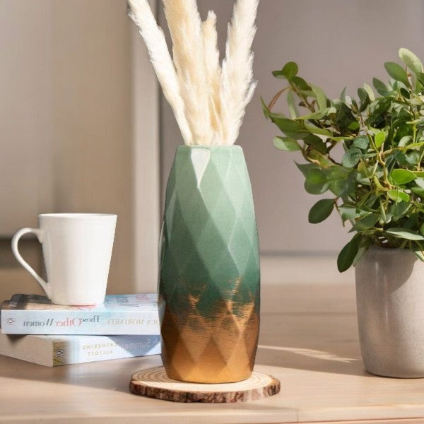 Green and gold faceted ceramic vase styled with dried stems on a table