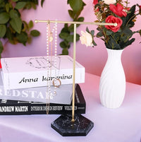 Gold T-bar necklace stand with black marble-effect base displaying jewellery beside flowers