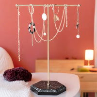 Necklaces hanging from gold T-bar stand on black hexagonal base