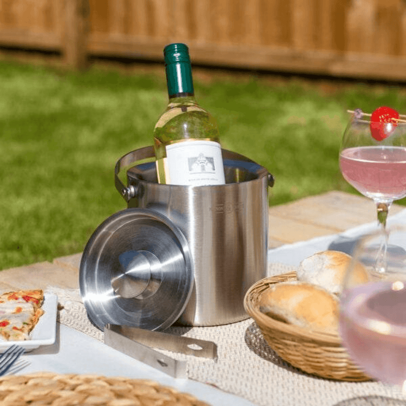 Stainless steel ice bucket styled with a wine bottle and drinks outdoors