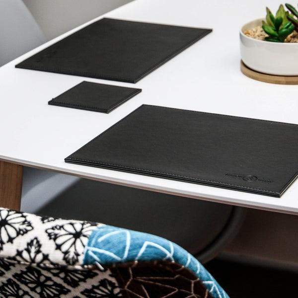 Black placemats and a matching coaster on a dining table