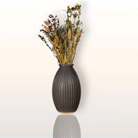 Black grooved stoneware vase holding a pale dried-flower arrangement