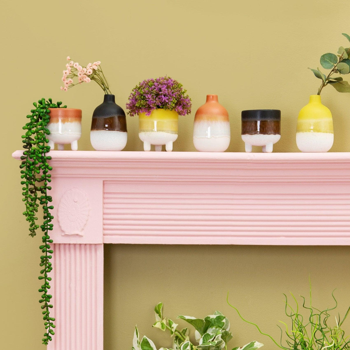 Assorted glazed vases and planters displayed on a pink mantelpiece