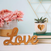 Freestanding gold Love decoration displayed beside books and a plant