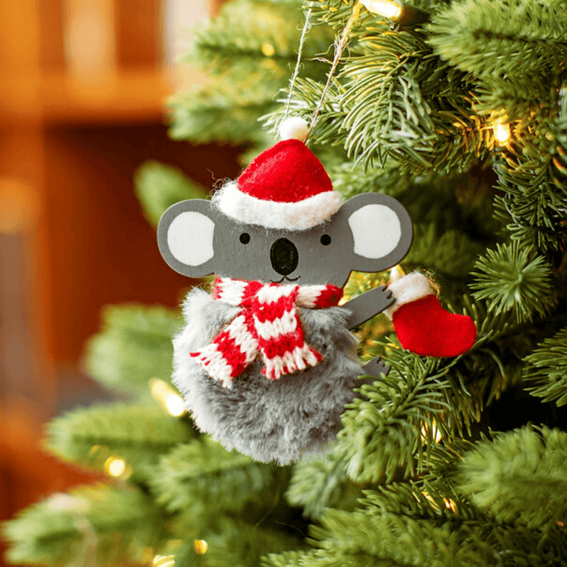 Festive koala ornament with fluffy grey body, Santa hat and striped scarf hanging on a Christmas tree