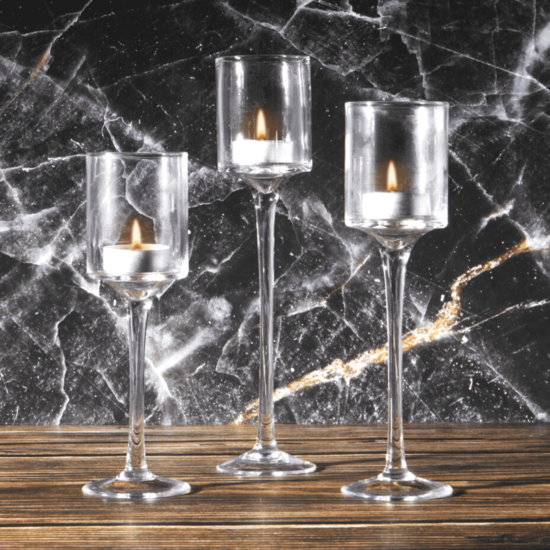 Three tall clear glass tealight holders with lit candles against a dark marble background