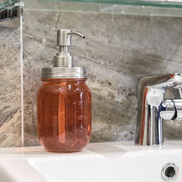 Glass mason jar soap dispenser filled with amber liquid beside a bathroom tap