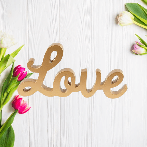 Gold Love script word decoration on a pale wooden background with flowers