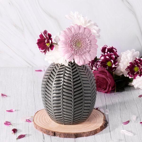 Grey leaf-patterned ceramic vase holding pink and burgundy flowers