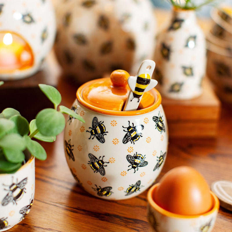 Busy Bee honey jar with yellow lid and striped spoon styled on a kitchen worktop