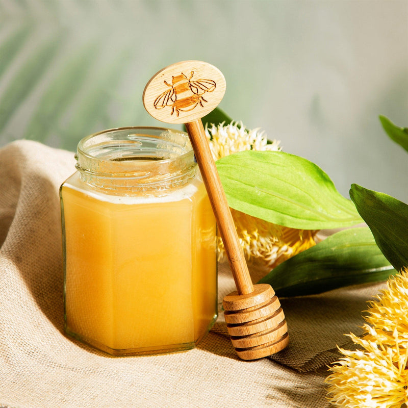 Bee engraved bamboo honey dipper beside an open jar of honey