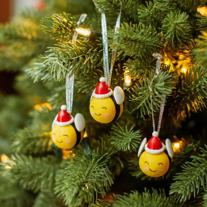 Three yellow and black bee Christmas decorations with red Santa hats hanging on a tree