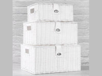 Three white woven storage baskets with lids stacked against a pale wall